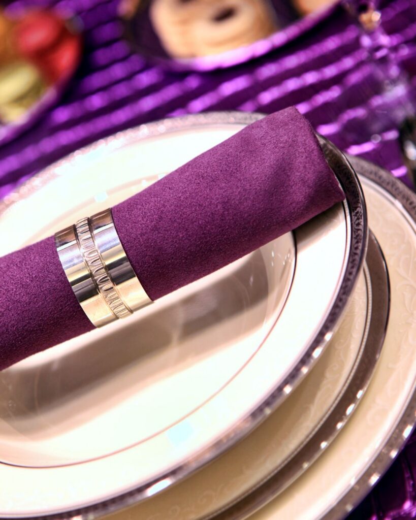 Purple rimmed white dishes with a purple napkin in the center with a napkin ring.